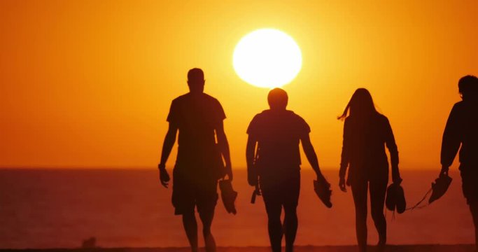 Silhouettes of people walking towards sun on a beautiful sunset beach. 4K UHD.