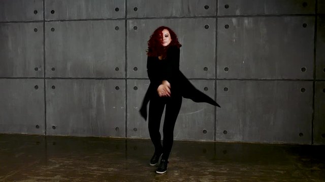 Young red-haired woman performs in black clothes near wall