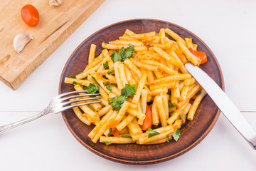 Macaroni with red sauce in a clay dish on a rustic light background - vegetarian recipe with tomatoes