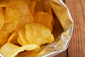Potato chips in a silver package on a wooden background close-up.