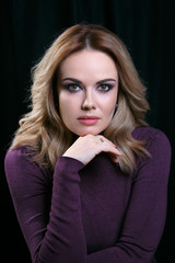 Portrait of beautiful model with curly light hair on black background. A hand rested to her chin.