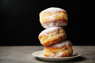 A stack of three sufganiyot donuts with jelly on black background - obrazy, fototapety, plakaty