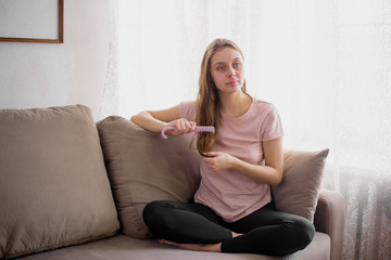 Portrait of attractive young woman sitting on couch at home, applying a cream, for saving her skin