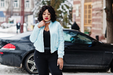 Fototapeta na wymiar Stylish african american plus size model with mobile phone at hand at winter snowy day against black car.