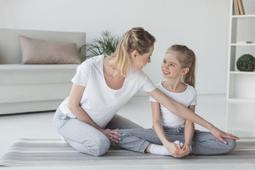 Fototapeta na wymiar mother teaching daughter how to sit in yoga butterfly pose