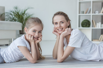 happy mother and daughter lying on floor together and looking at camera