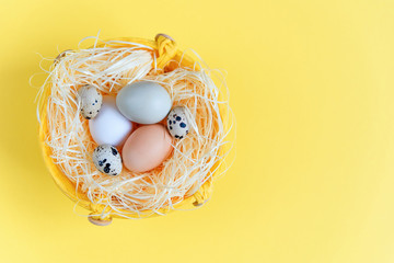 Easter eggs of different colors and quail eggs in a wicker basket on a yellow background, Top view. Flat lay. Easter concept.