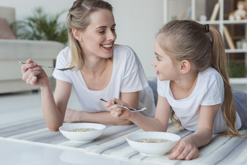happy mother and daughter eating cereal meal while lying on yoga mats