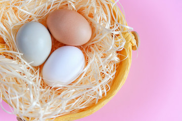 Easter eggs of different colors in a wicker basket on a pink background, Top view, Flat lay. Easter concept.