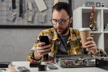 repairman using smartphone while holding coffee in hand