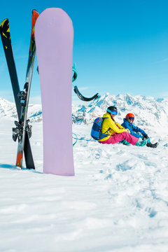 Photo of snowboard, skis on background of sitting sports woman and man on snowy hill