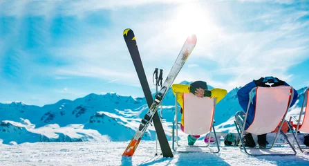 Fotobehang Image from back of vacationers in armchair, skis, sticks in snowy resort © Sergey