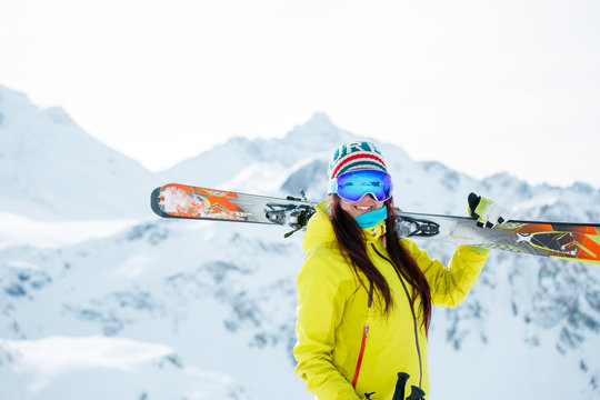 Image of female athlete with skis on her shoulder against background of snowy hill