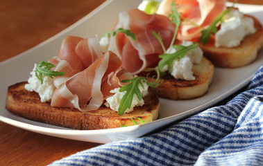 Bruschetta with ricotta, prosciutto, rucola on white plate
