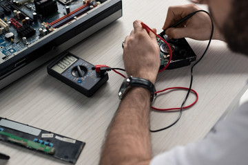 cropped image of man using multimeter with testing hard disk drive