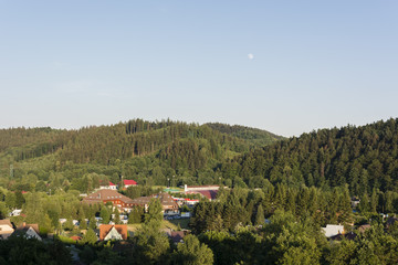 View of forested hills with moon in the sky during the day.