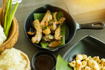 Isaan Food, charcoal-boiled pork neck in black pan on dark wooden table.