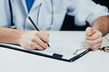 The doctor writes, large hands, near a stethoscope in the hospital