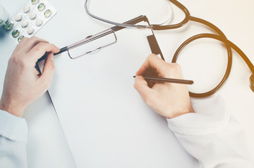 The doctor writes, large hands, near a stethoscope in the hospital