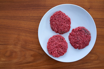 Three Raw Beef Steaks On a White Plate On a Wooden Table