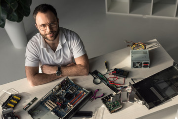 smiling man with crossed hands on table looking at camera