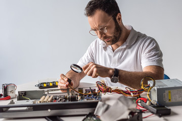 man using magnifier while holding wires in hand