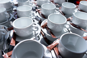 Many rows of white tea cups with saucer and sugar sticks on table