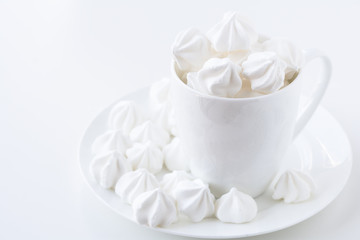 The side view of the white meringue in the white tea cup on the white plate on white table and white background