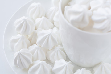 The side close up view of the white little meringue in the white tea cup on the white plate on white next to the white tea cup table and white background