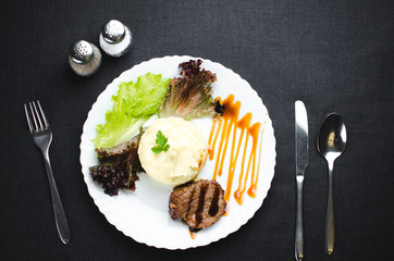On a white plate, on a beautiful fabric and dark background mashed potatoes with beef meat beautifully polished balsamic sauce