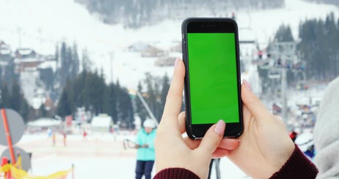 close-up female hand using smart phone digital device green screen chroma-key mock up content mountains winter tapping ski lift people skiing technology internet connect 3G scrolling touchscreen