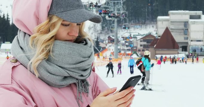 portrait attractive lady using smart phone winter holidays snowy mountain ski resort vacationland warm clothes cute pretty blonde woman cap jacket business email touchscreen app notification beauty