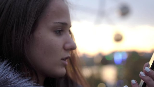 Attractive brunette young woman using mobile phone on streets of night town with beautiful lights bokeh. Slow motion. 3840x2160