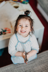 Fototapeta premium toddler girl in drawing apron draws fingers at home, smiling on the camera