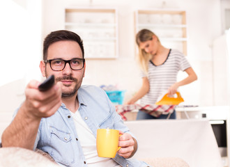Man watching tv and woman doing housework
