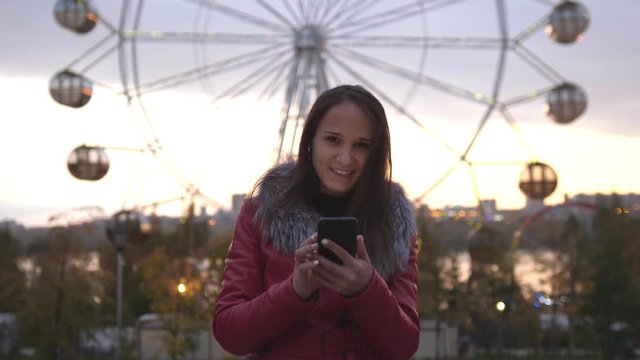 Pretty brunette young woman using mobile phone during walk on streets of night town with beautiful lights bokeh. 3840x2160, slow motion