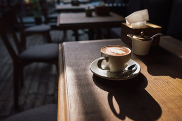 A cup of coffee on the wood table and sunlight