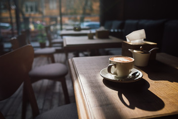 A cup of coffee on the wood table and sunlight with cozy cafe interior background