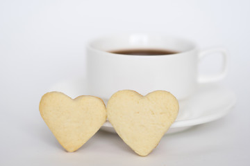 Tea cup with saucer and two heart shape cookies on white background.  Valentine's Day concept.