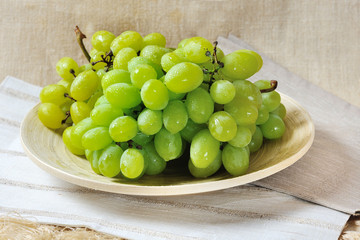 Bunch of sweet juicy green grapes on a wooden plate