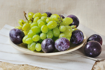 Bunch of sweet juicy green grapes and plums on a wooden plate
