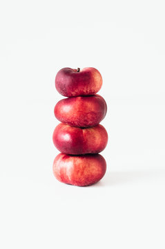 Stack of fresh flat donut nectarines, red saturn nectarines or ripe fuzzless vineyard peaches on white background
