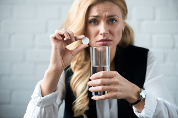 businesswoman holding pill and glass of water and looking at camera