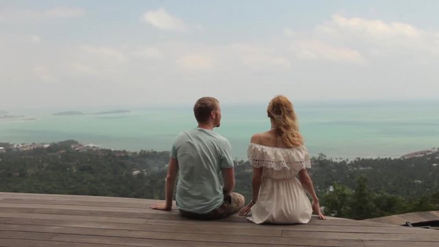 young couple sitting on a cliff overlooking a tropical island