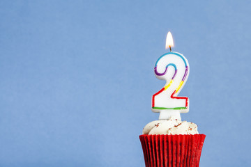 Number 2 birthday candle in a cupcake against a blue background