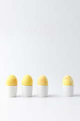 four yellow painted easter eggs in egg stands on white