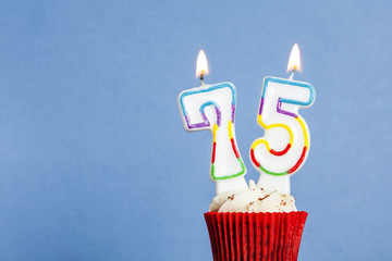 Number 75 birthday candle in a cupcake against a blue background