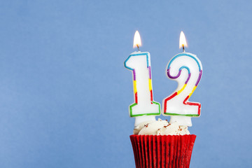 Number 12 birthday candle in a cupcake against a blue background