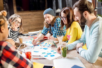 Group of caucasian coworkers dressed casually working together with documents and laptops at the big table in the beautiful cafe interior