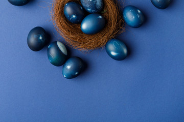 top view of blue painted easter eggs in decorative nest on blue surface